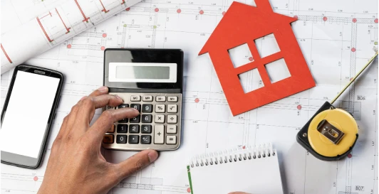 A model house, calculator and measuring tape laid over architectural floor plans