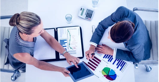 Two professionals comparing financial charts and a tablet during a transaction review