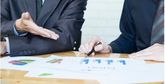 Two professionals discussing a compliance report across a table