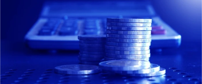 Stacked coins in front of a calculator in blue light