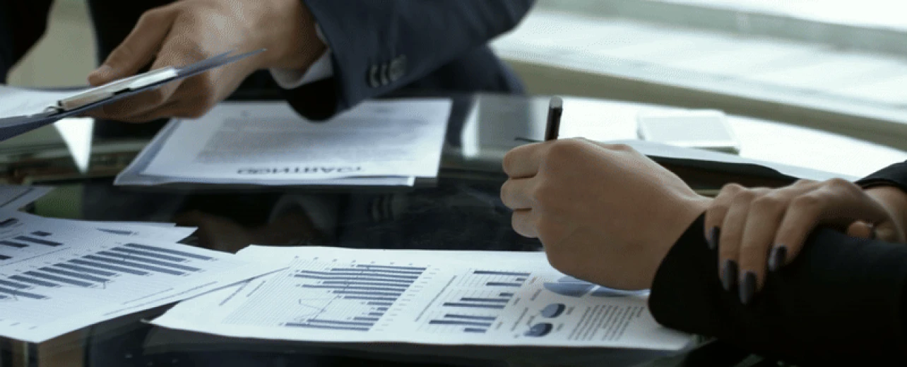 Two professionals reviewing a signed contract and charts at a glass desk