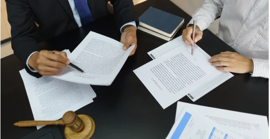 Two professionals reviewing legal documents at a desk beside a gavel